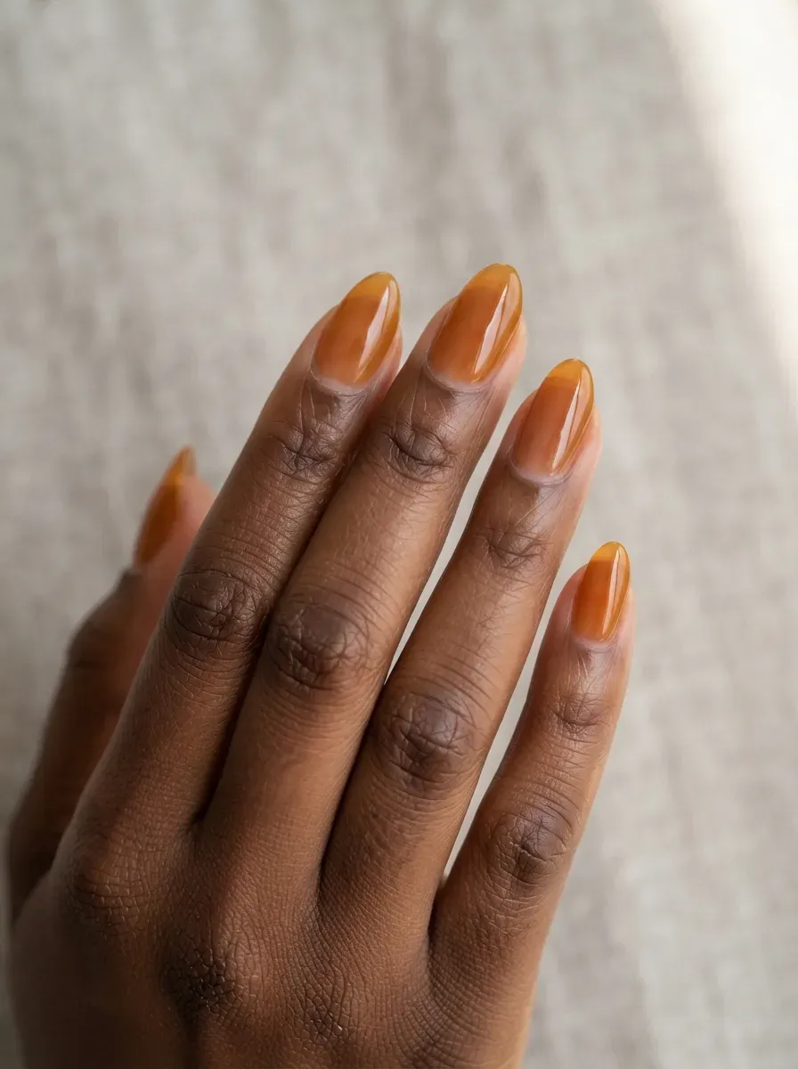 Close-up of medium almond nails with amber glass jelly polish on warm brown skin