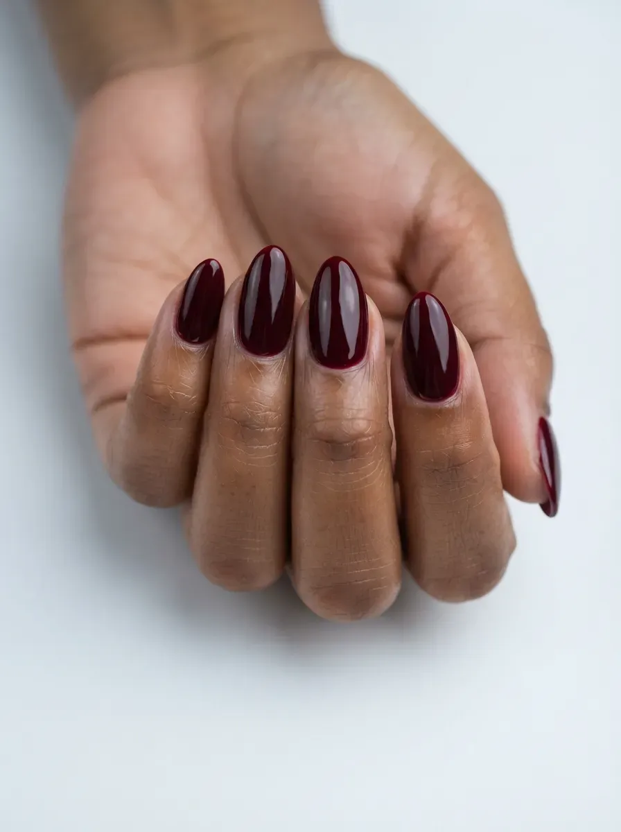 Close-up of medium almond nails in glossy black cherry polish on deep brown skin