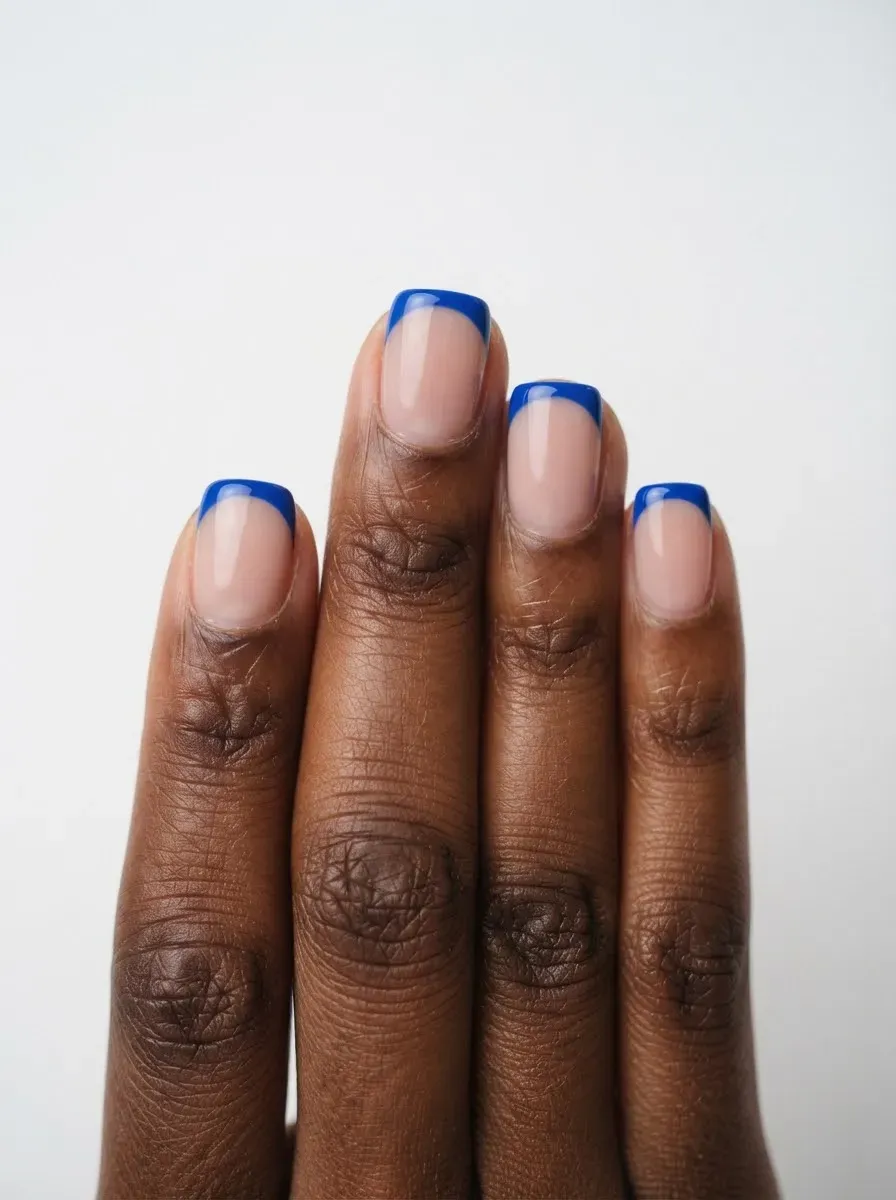 Close-up of short nails with blue French tips on deep brown skin