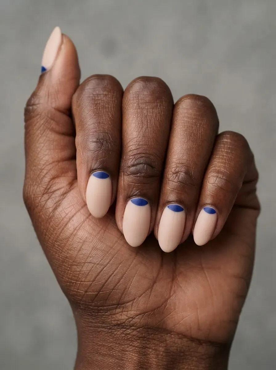 Close-up of nude nails with blue half-moon accent on deep chestnut skin