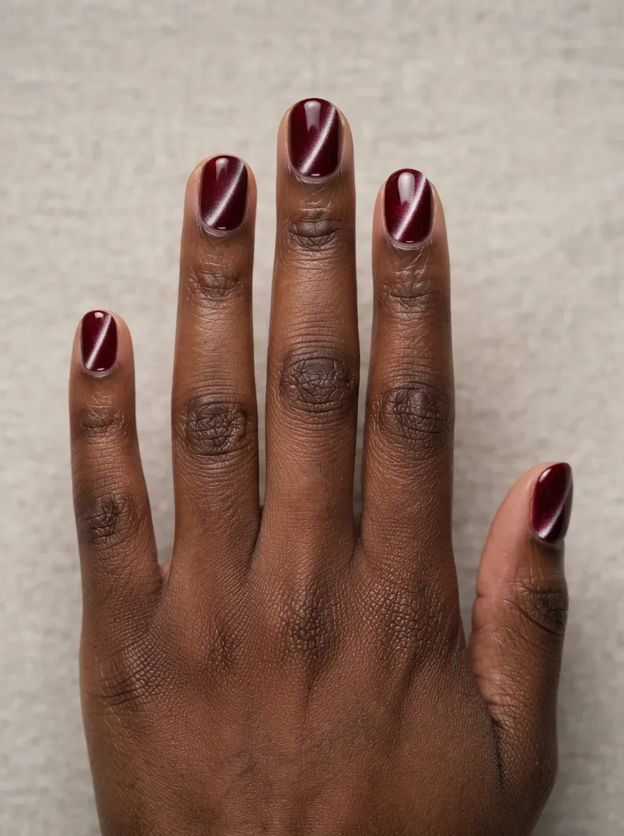 Short round nails with bordeaux cat-eye polish and side stripe on rich dark skin