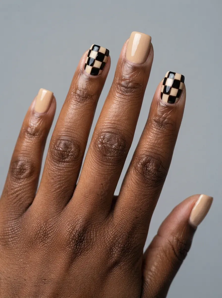 Close-up of square nails in cream with black checkerboard accent nails