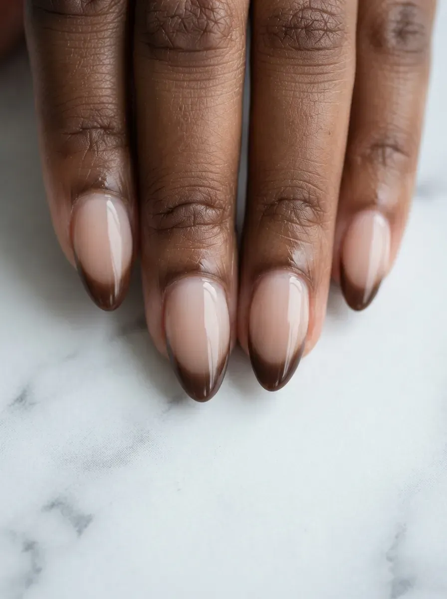 Close-up of medium almond nails with chocolate brown french fade tips on warm brown skin