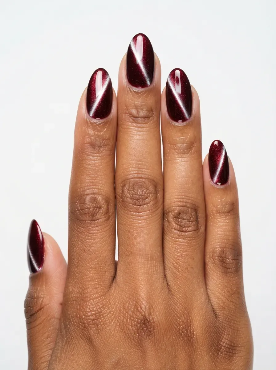 Almond nails with chrome cherry cola cat-eye polish and mirror stripe on warm brown skin