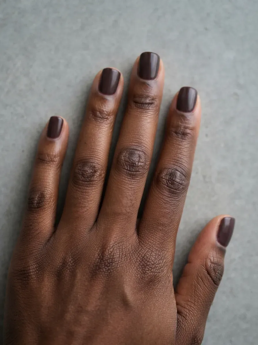 Close up of very short squoval nails with deep plum polish on deep brown skin