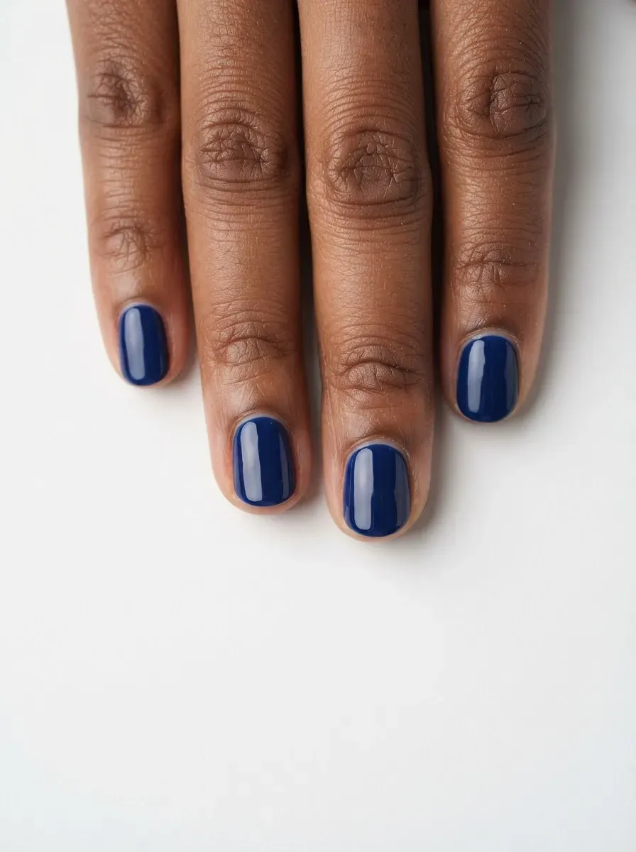 Close-up of short round nails in deep sapphire on brown skin with warm undertones