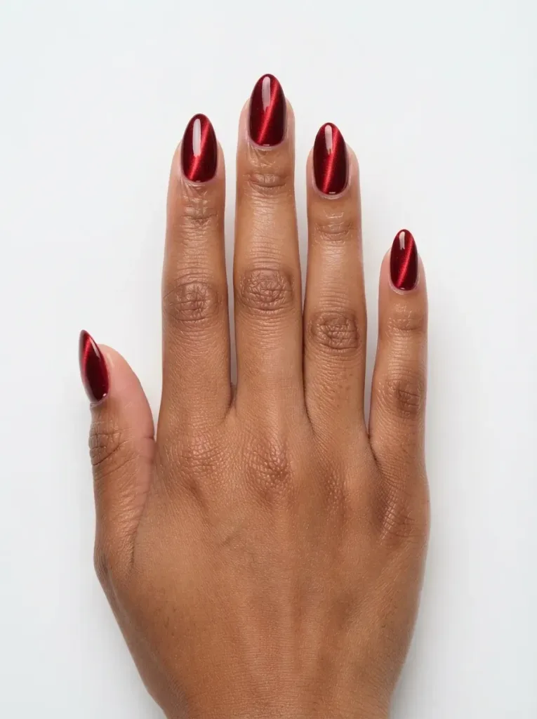 Almond nails with deep scarlet cat-eye polish and clean center stripe on warm brown skin