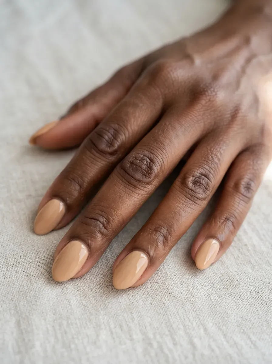 Close up of short almond nails in honey beige polish with glossy finish