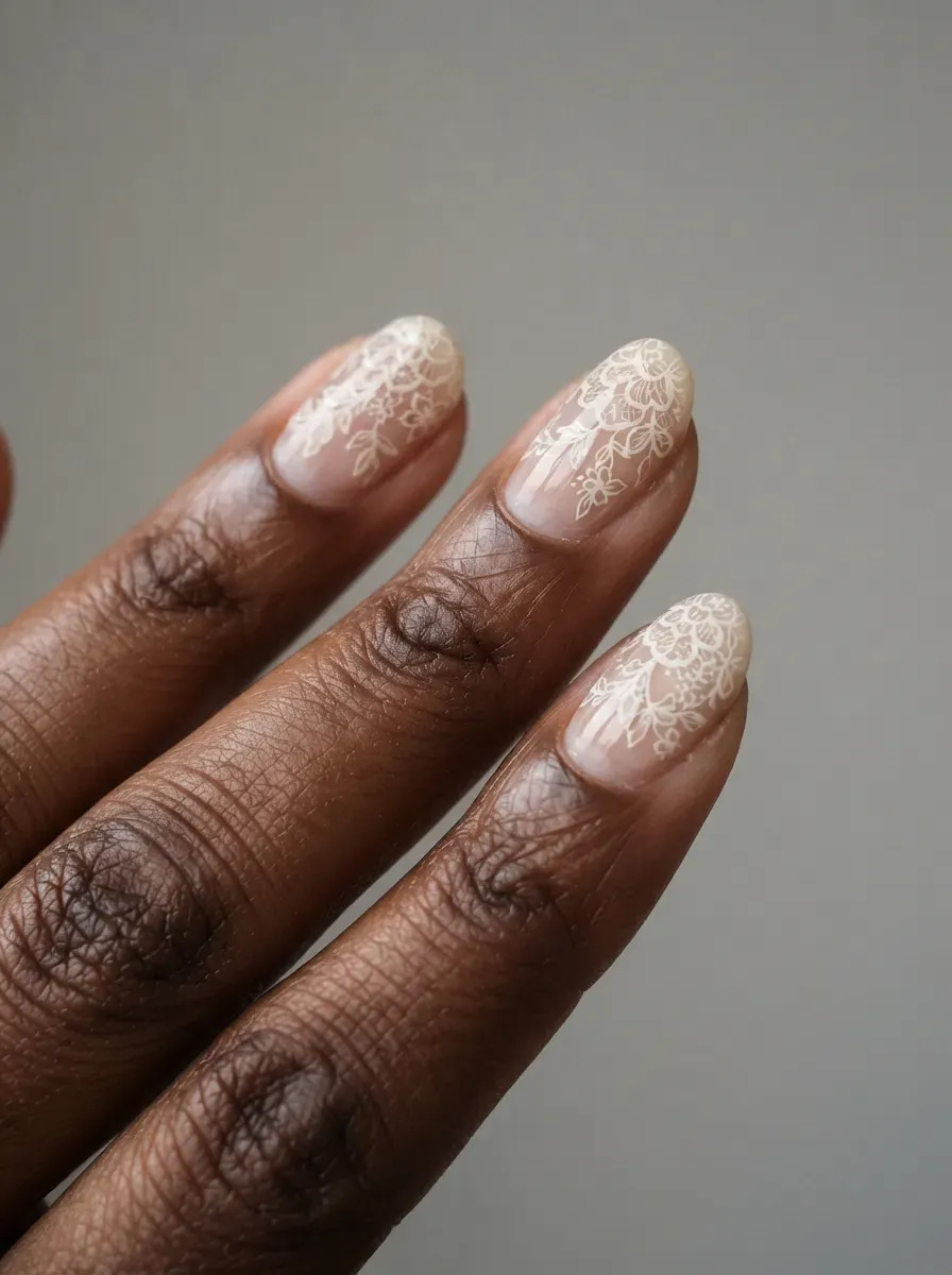 Close-up of oval nails with ivory lace over a sheer base on rich dark skin