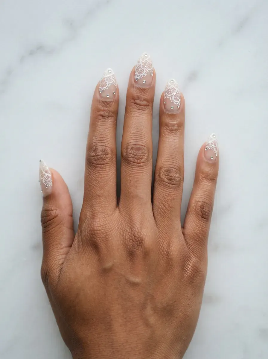 Close-up of almond nails with white lace dotted with micro crystals on brown skin
