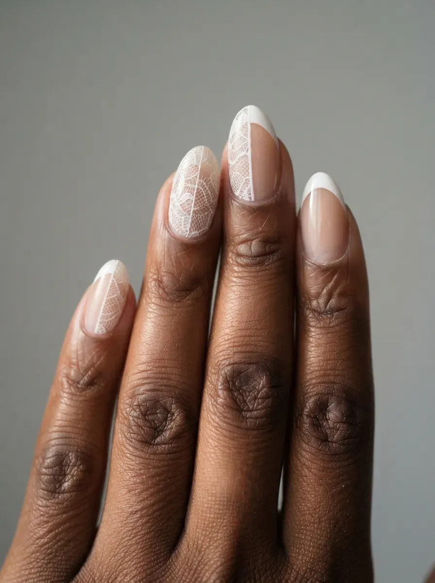 Close-up of almond nails with white lace crescent along one sidewall on warm brown skin