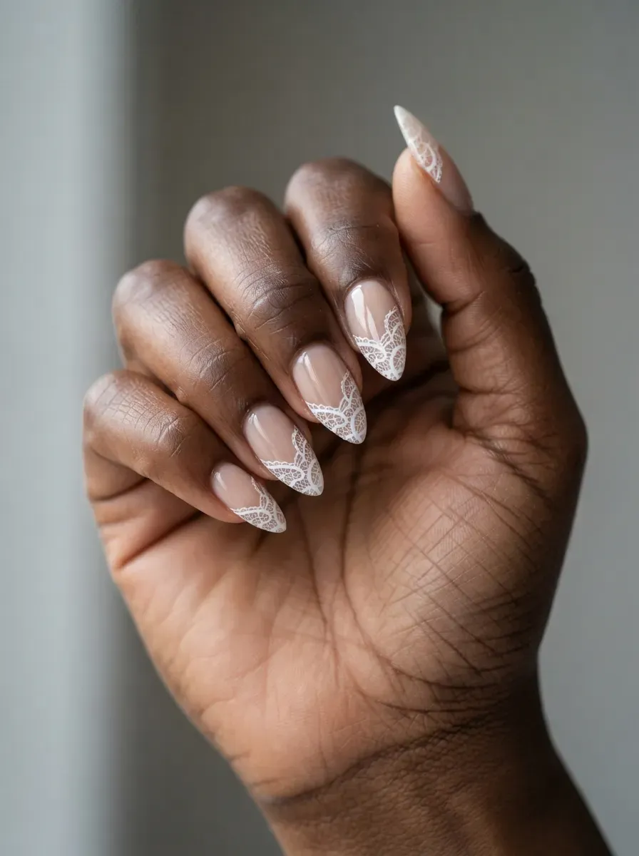 Close-up of stiletto nails with white lace tips over nude polish on rich dark skin