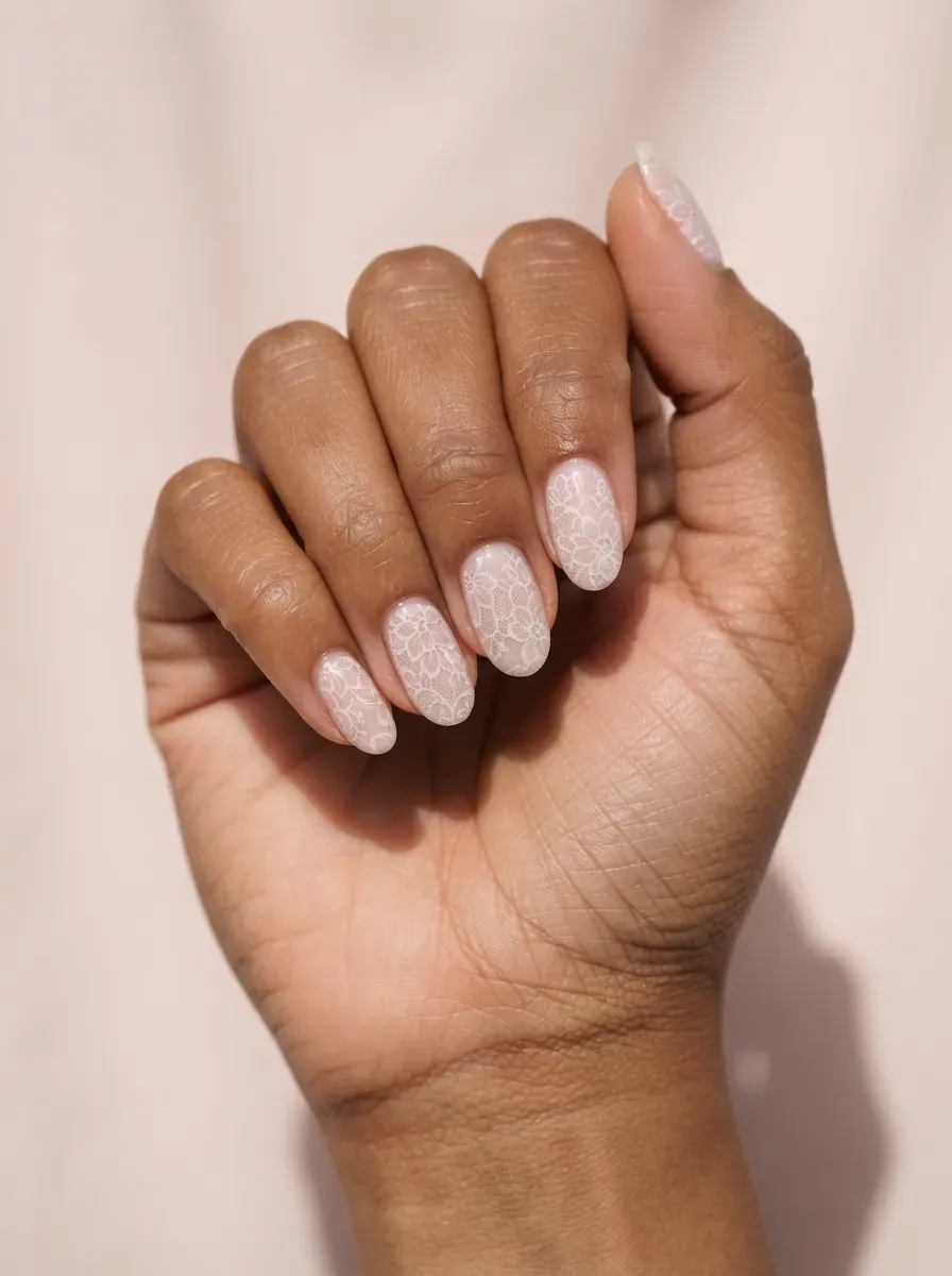 Close-up of oval nails with faint lace under a milky wash on warm brown skin