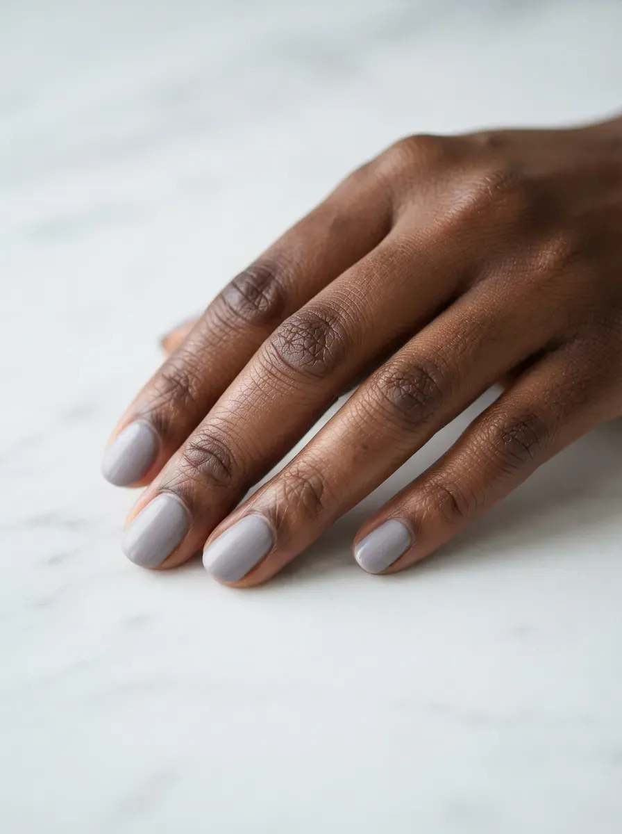 Close up of short oval nails with lavender gray cream polish on deep chestnut skin