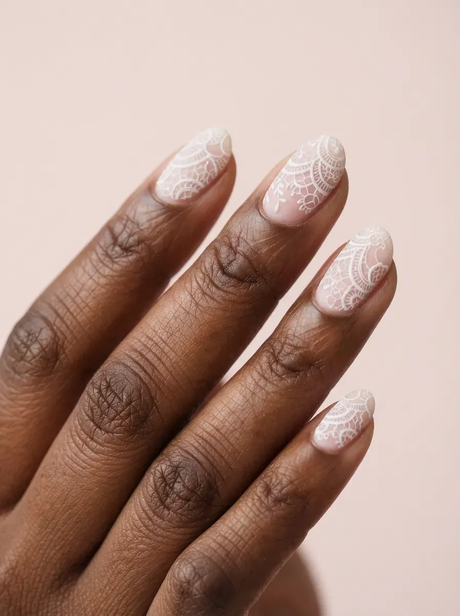Close-up of oval nails with matte white lace over blush polish on rich dark skin