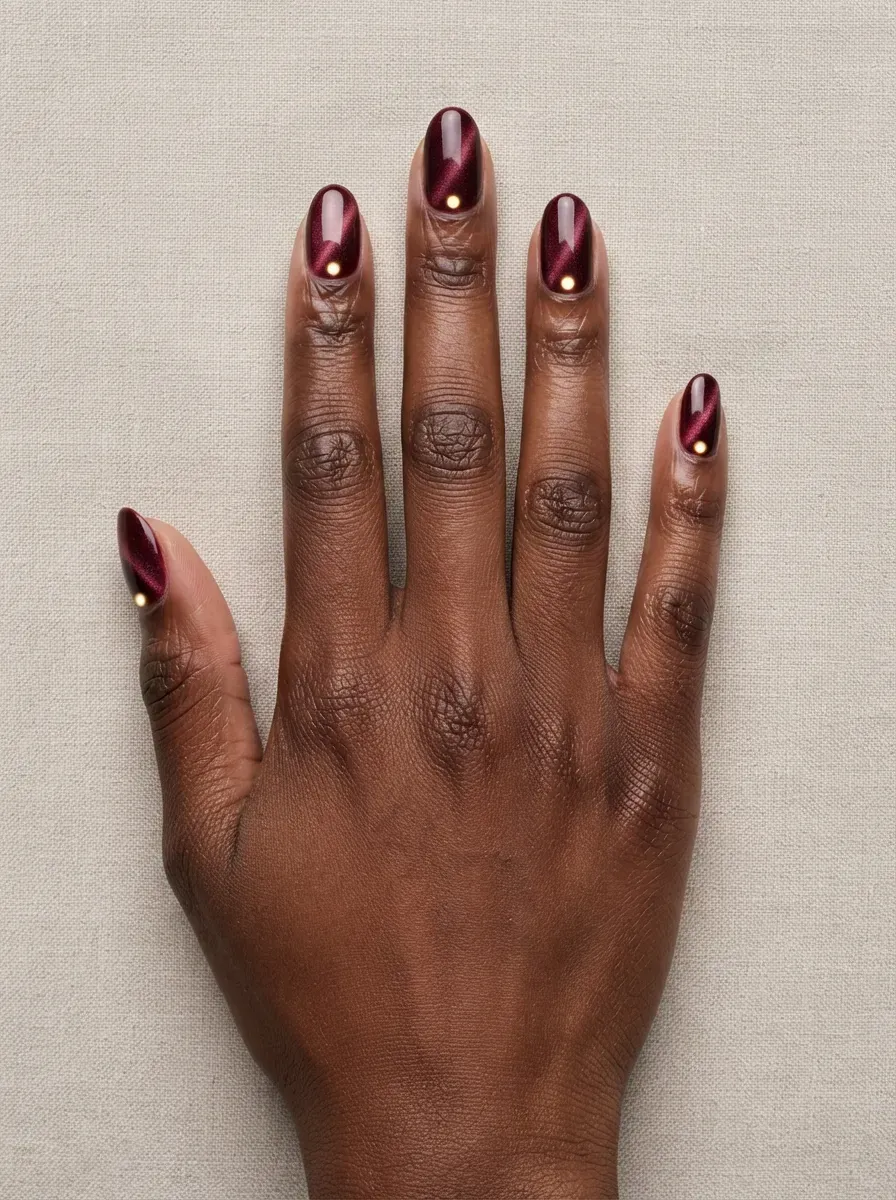 Oval nails with merlot cat-eye polish and glowing dots near cuticles on deep chestnut skin