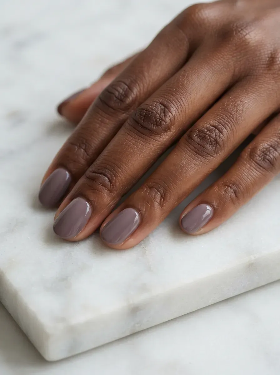 Close up of short oval nails with muted mauve polish on deep chestnut skin