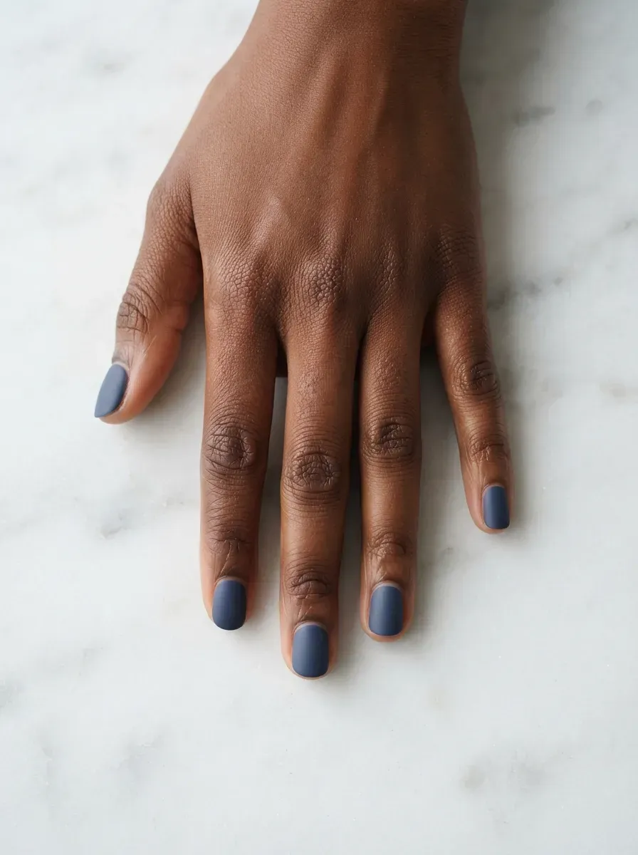 Close up of very short nails with muted navy polish on deep chestnut skin