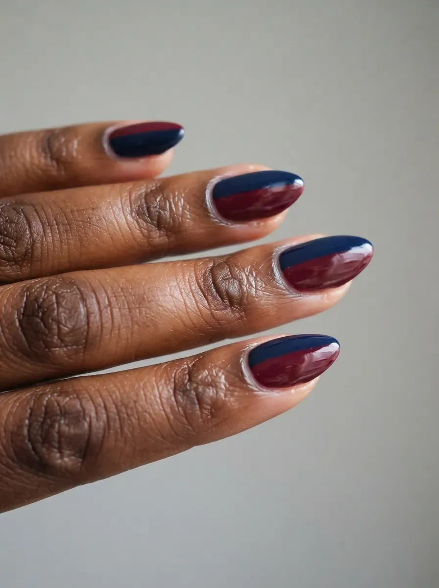 Close-up of medium almond nails with navy and burgundy halves on rich dark skin