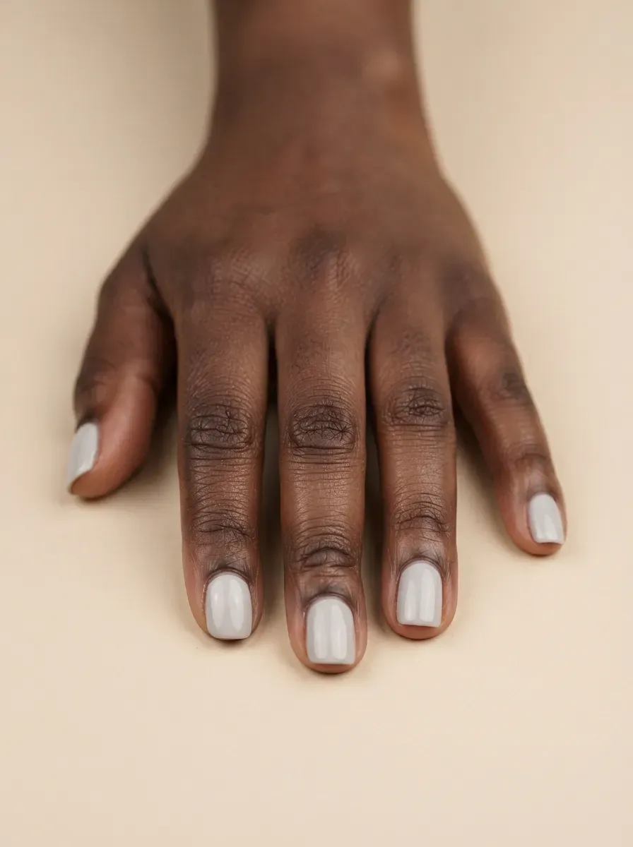 Close up of short squoval nails with pale gray cream polish on deep brown skin