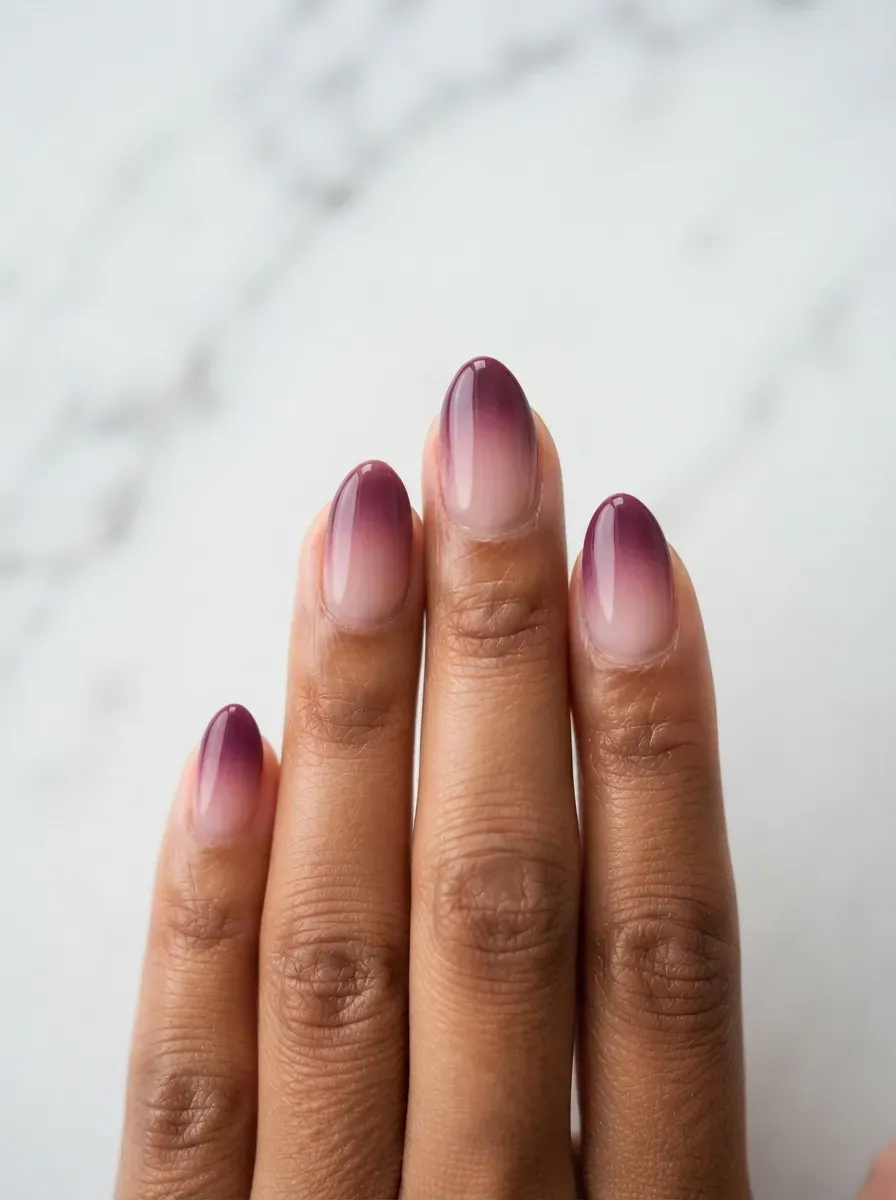 Close-up of medium almond nails with plum aura ombre blending on deep brown skin