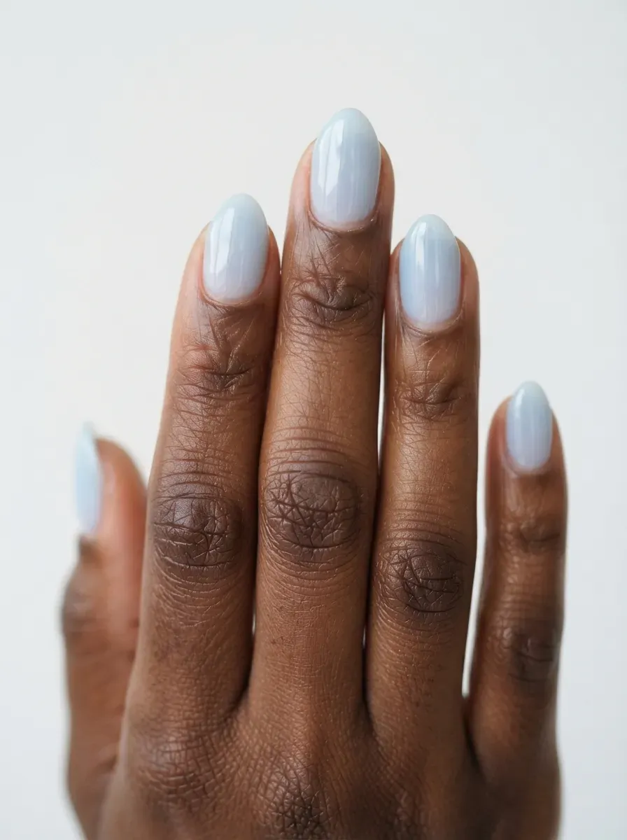 Close up of short almond nails in sheer powder blue polish with glossy finish