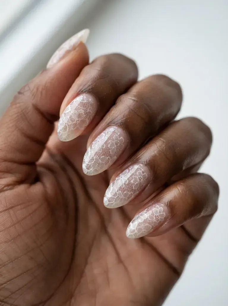 Close-up of almond nails with white lace sealed under clear gel on deep brown skin