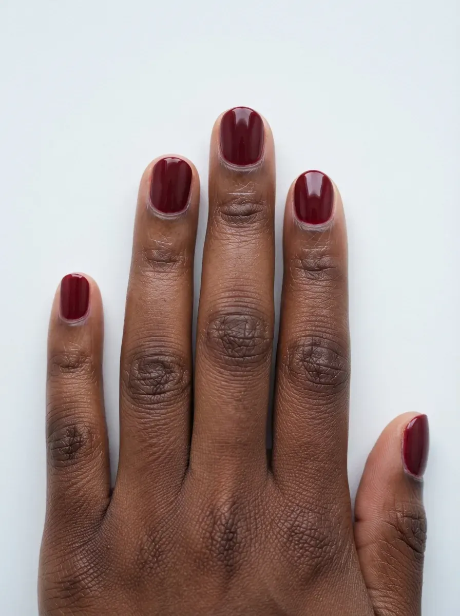 Close-up of short round nails in rich merlot glossy polish on warm brown skin