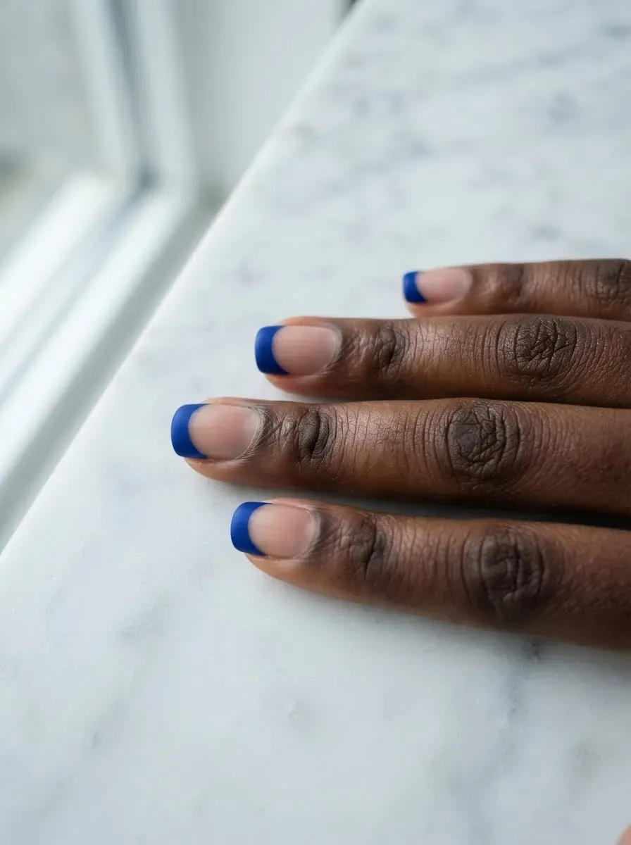 Close-up of short nails with bold blue tips on rich dark skin tone