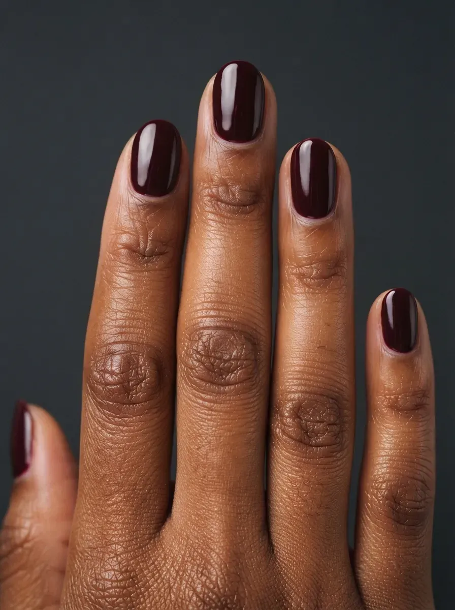 Close up of short oval nails with glossy burgundy polish on brown skin with warm undertones