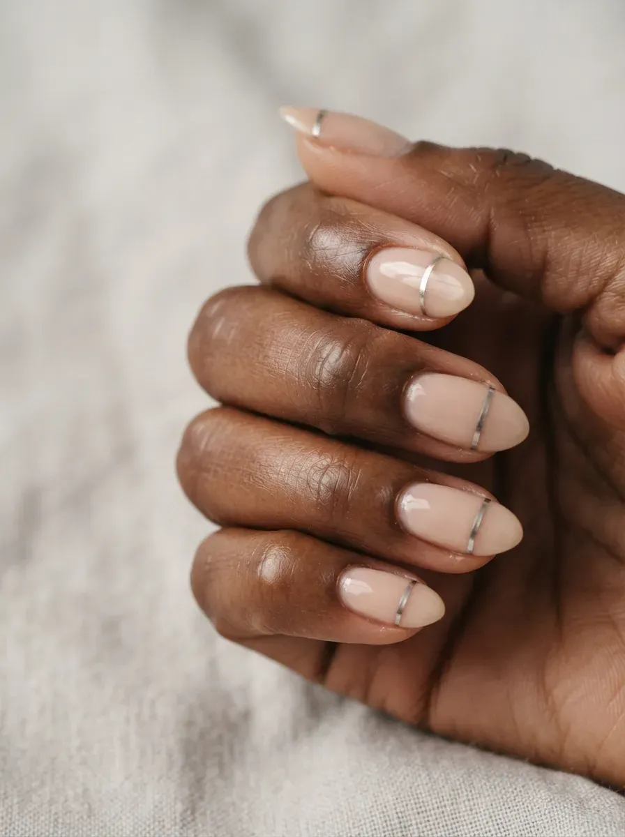 Close up of almond nails in sheer nude polish with one fine silver horizontal stripe