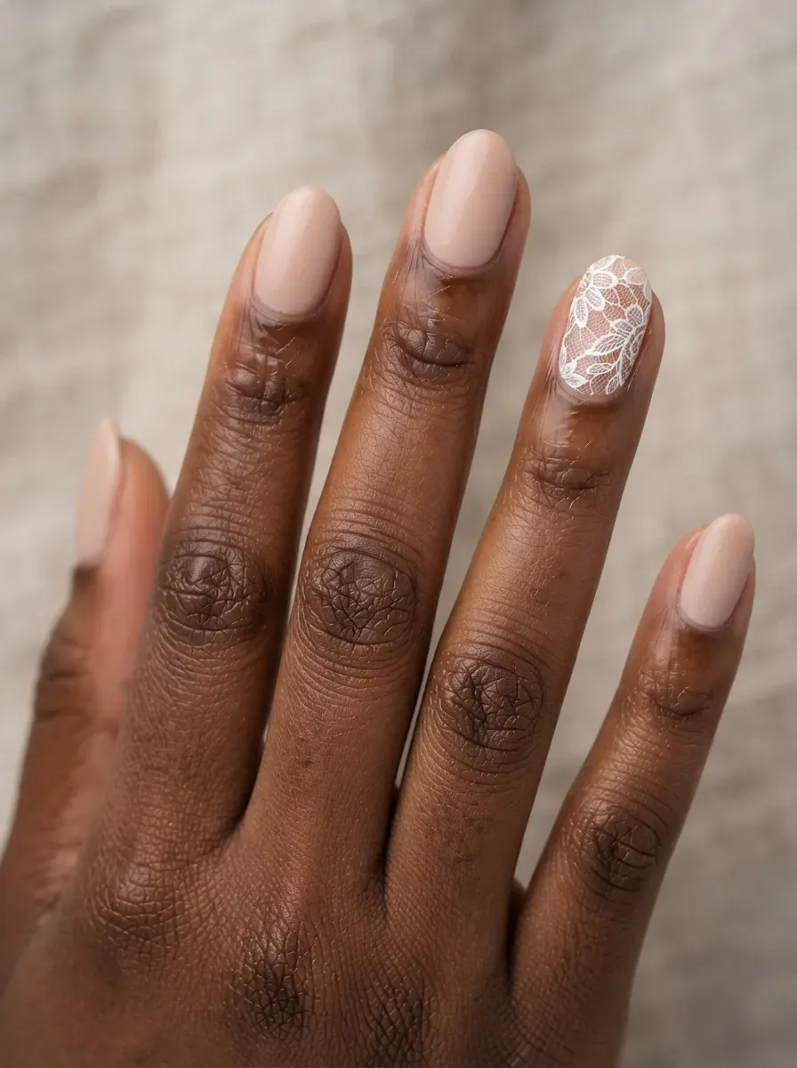 Close-up of nude nails with a single white lace accent nail on deep chestnut skin