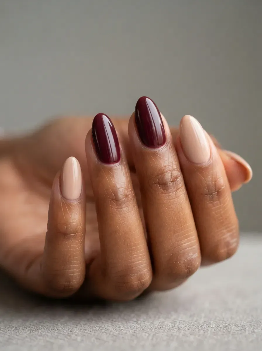 Close-up of medium almond nails with beige polish and burgundy accents on deep brown skin