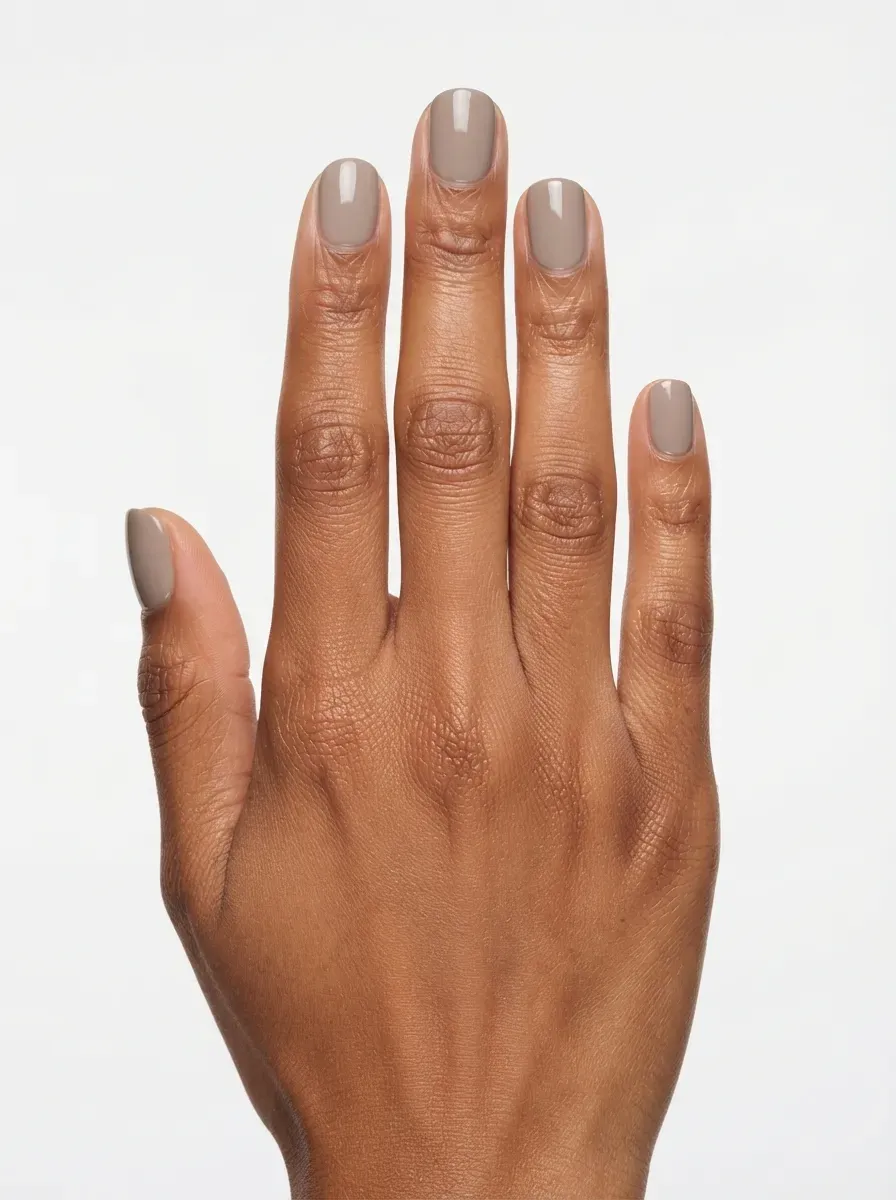Close up of short nails with taupe cream polish on brown skin with warm undertones