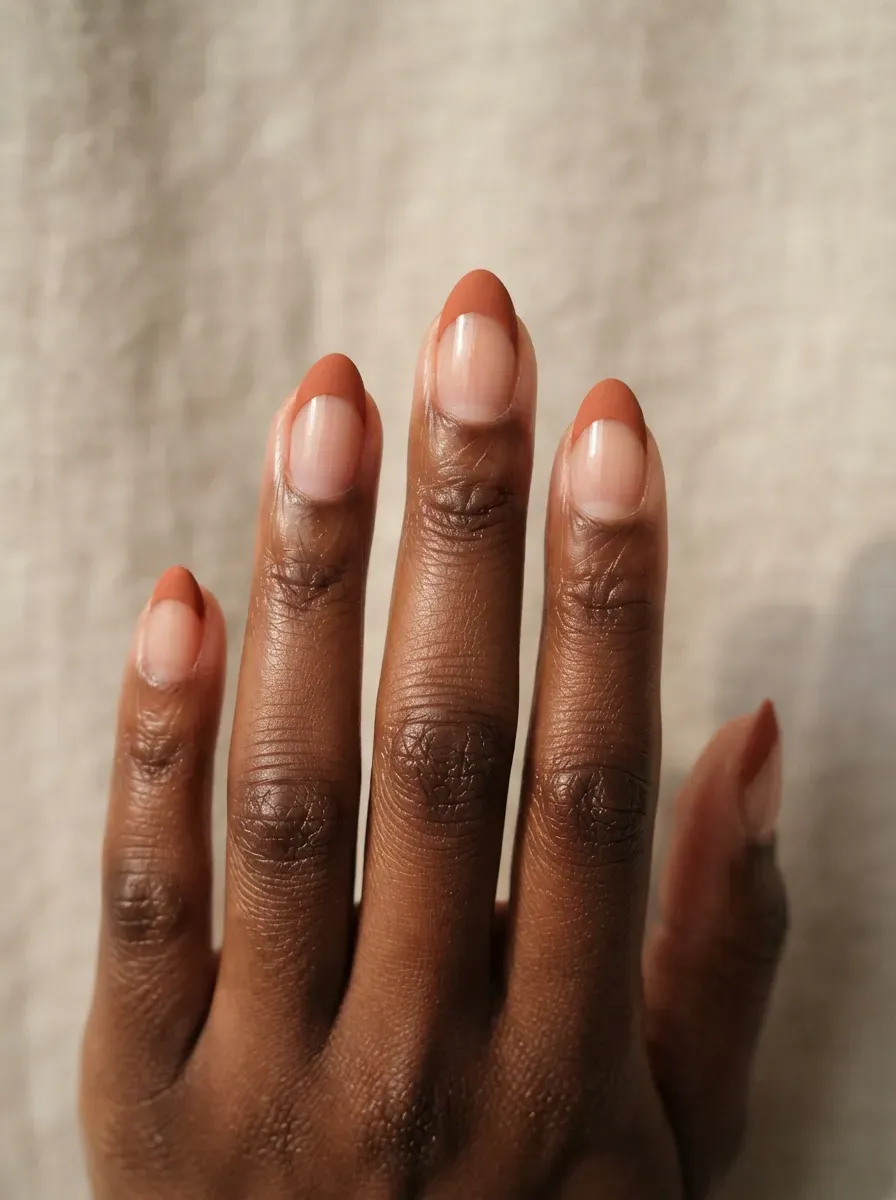 Close-up of short almond nails with terracotta matte french tips on rich dark skin