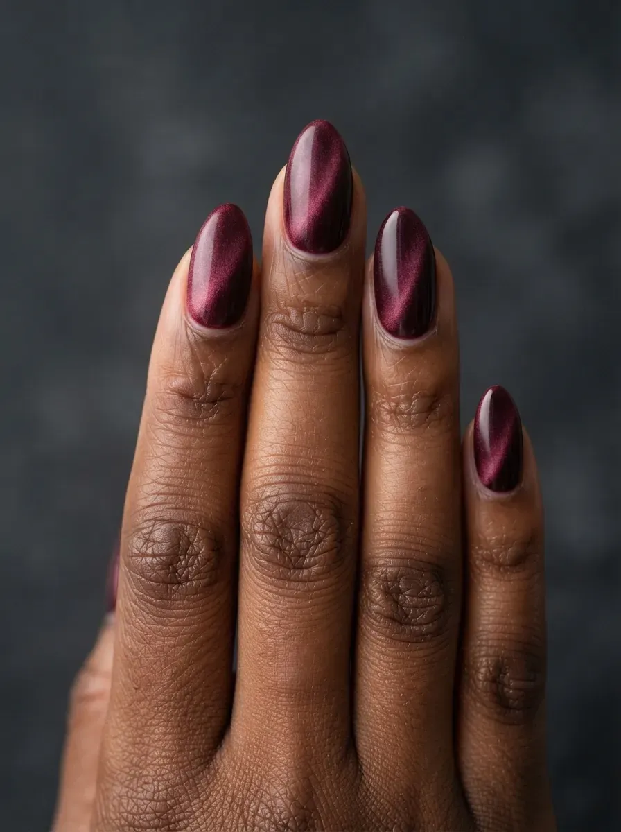 Almond nails with velvet plum-red cat-eye polish and even soft shimmer on deep brown skin