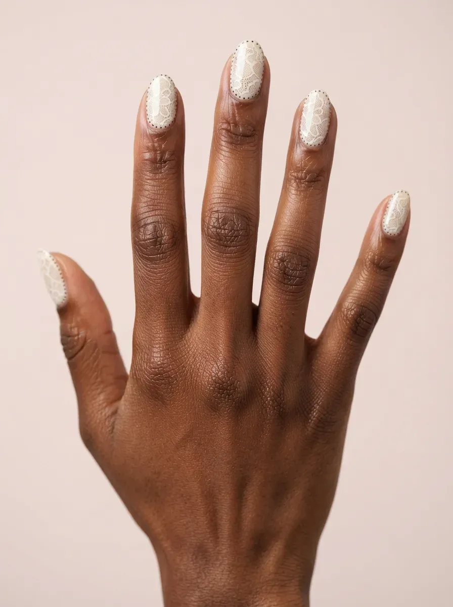 Close-up of oval nails with vintage white lace and dotted outlines on deep chestnut skin