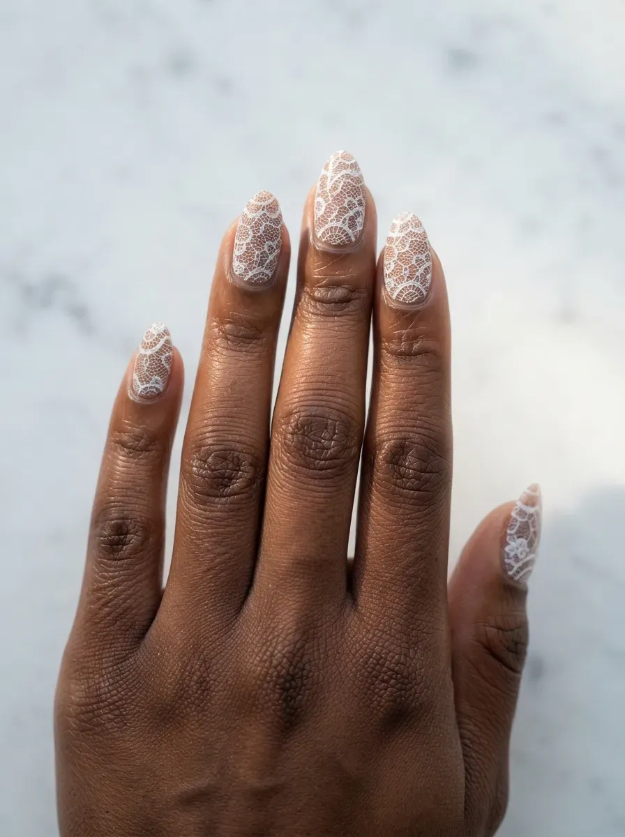 Close-up of almond nails with white lace over deep nude base on deep brown skin